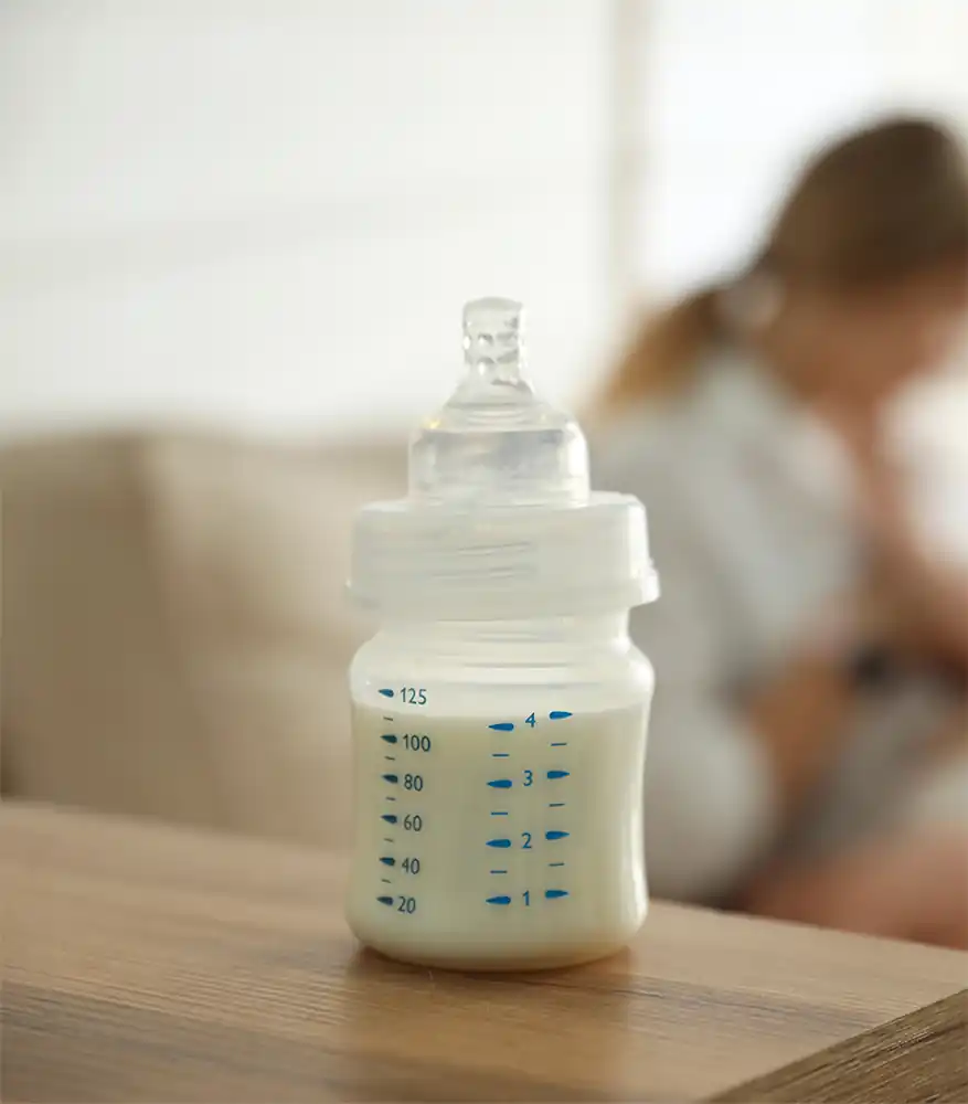 Eine Milchflasche und im Hintergrund eine stillende Mutter
